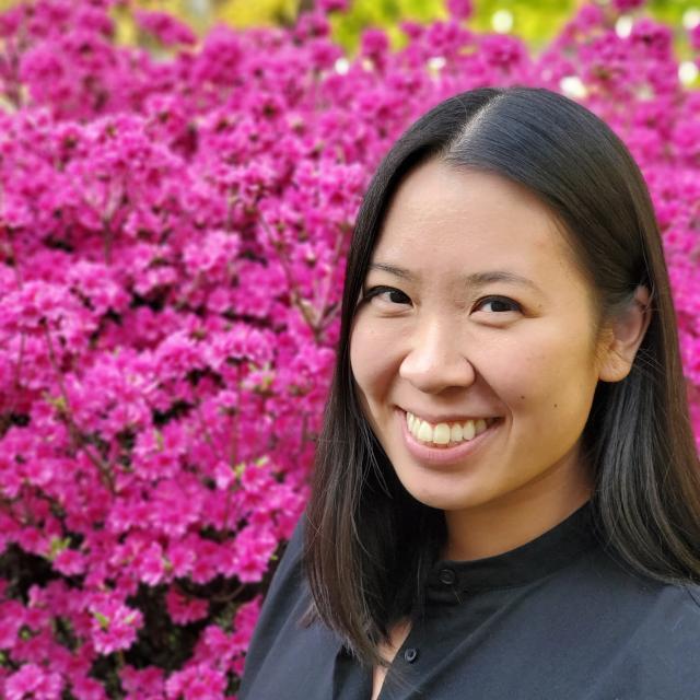 Jessica Peng poses for a portrait in front of flowering pink bush.